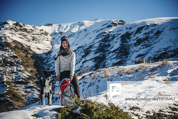Kaukasische Frau posiert mit Hund und Rucksack auf einem Berg