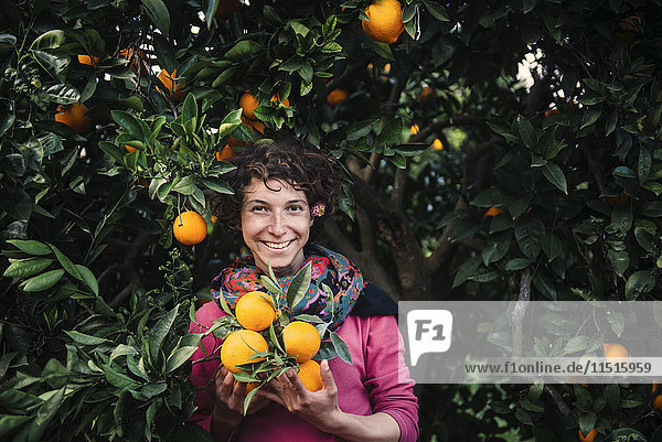 Lächelnde kaukasische Frau hält Orangen unter einem Baum