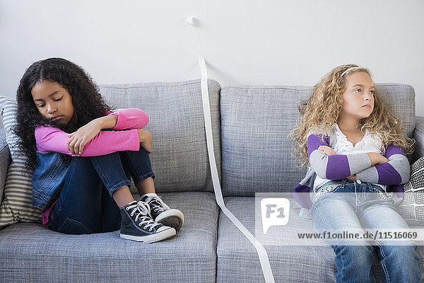 Frustrated girls dividing sofa with tape