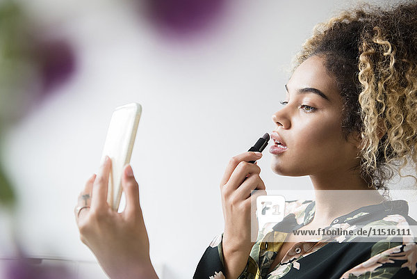 Mixed-Race-Frau hält Handy und trägt Lippenstift auf