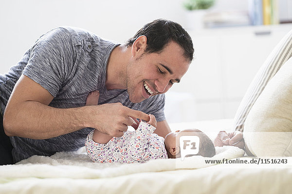 Hispanic father laying on bed playing with baby daughter