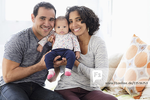 Hispanic mother and father posing with baby daughter