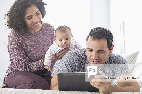 Hispanische Mutter und Vater mit kleiner Tochter  die auf ein digitales Tablet schauen