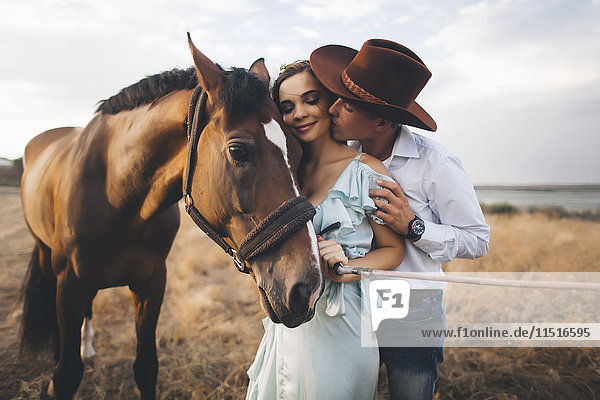 Kaukasischer Cowboy küsst Frau auf die Wange in der Nähe des Pferdes