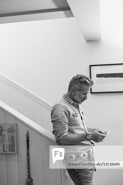 Caucasian man leaning on staircase bannister texting on cell phone
