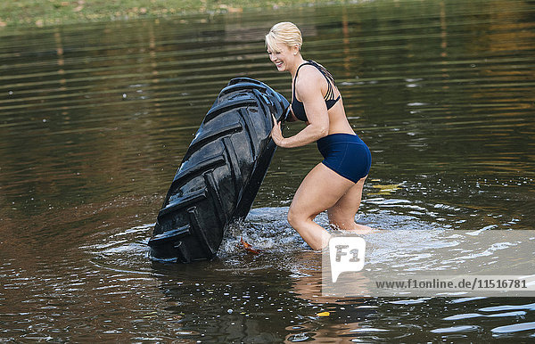 Kaukasische Frau  die einen schweren Reifen in einen See schiebt