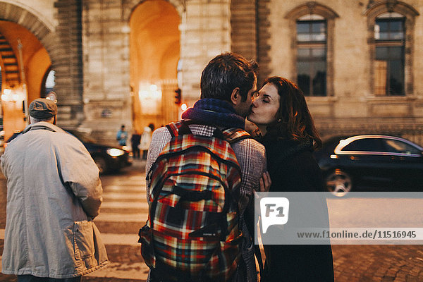 Caucasian woman kissing man on cheek in city at night