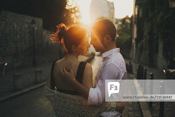 Caucasian couple hugging in city street at sunset