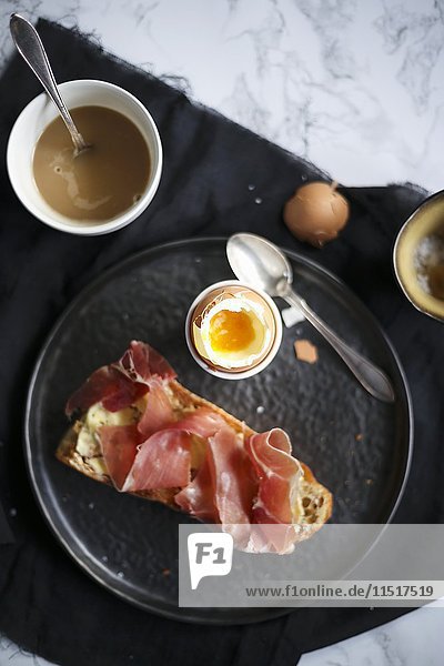 Frühstück mit einem weichgekochten Ei und Brot mit Schinken