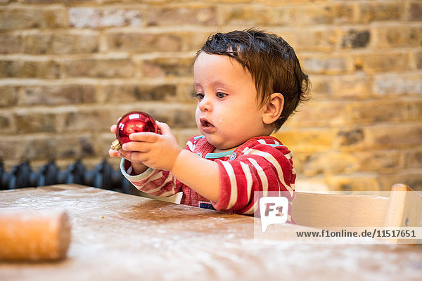 Kleiner Junge spielt mit Weihnachtskugel bei Tisch