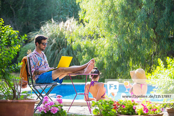 Man poolside with feet up using laptop computer
