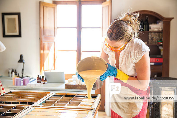 Junge Frau gießt flüssige Lavendelseife in einer Werkstatt für handgemachte Seife in Gussformen