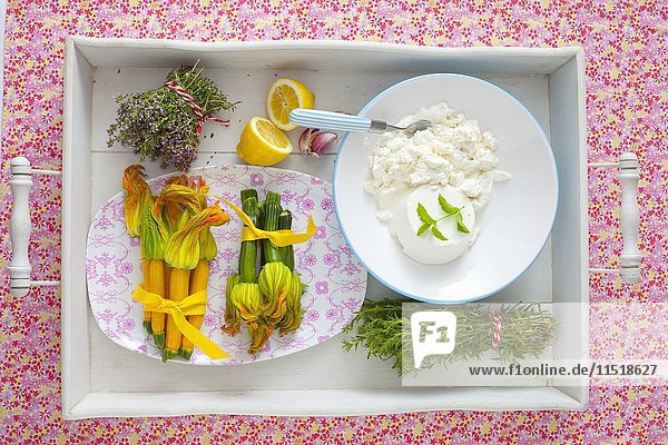 Ein Arrangement aus Zucchiniblüten  frischen Kräutern und Ricotta auf einem Tablett