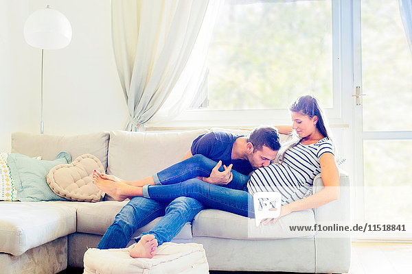 Mann auf Sofa küsst schwangere Frau auf den Bauch