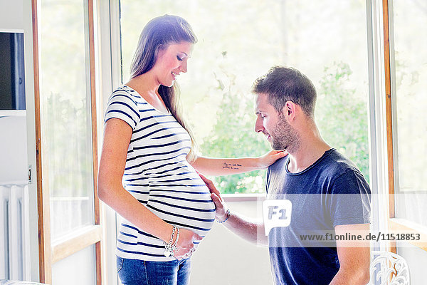 Mann berührt lächelnd den Bauch einer schwangeren Frau