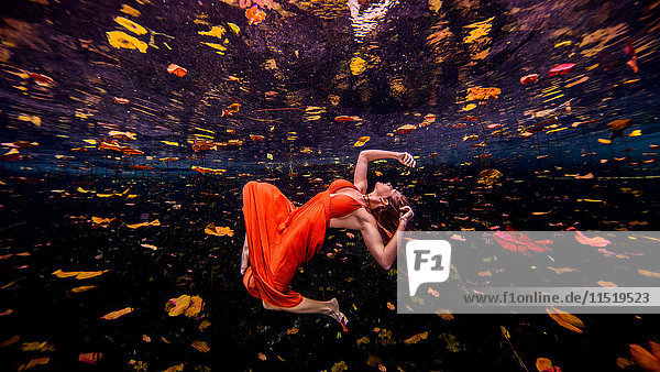 Frau in orangem Kleid  schwimmt zur Wasseroberfläche  Unterwasseransicht