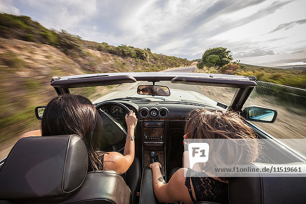 Two young women in convertible car  driving along scenic road  rear view