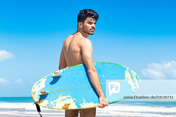 Junger Mann steht am Strand und hält ein Surfbrett  Fortaleza  Ceara  Brasilien