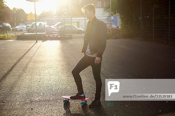 Junger männlicher Skateboarder mit Skateboard auf sonnenbeschienener Strasse
