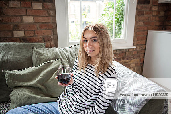 Porträt einer jungen Frau  die auf einem Sofa sitzt und ein Glas Wein hält