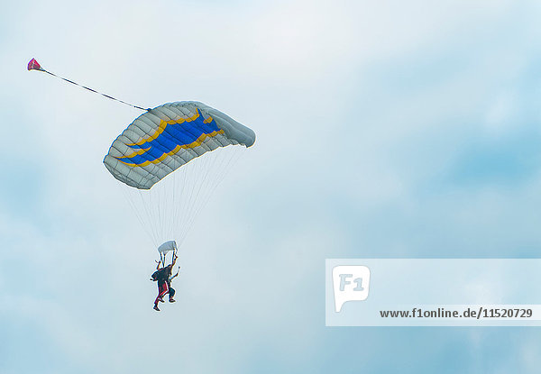 View of tandem parachuting down against cloudy sky