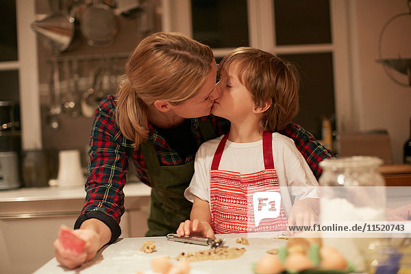 Frau küsst Sohn beim Backen an der Küchentheke