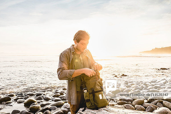 Man searching backpack at beach in Juan de Fuca Provincial Park Vancouver Island British Columbia Canada