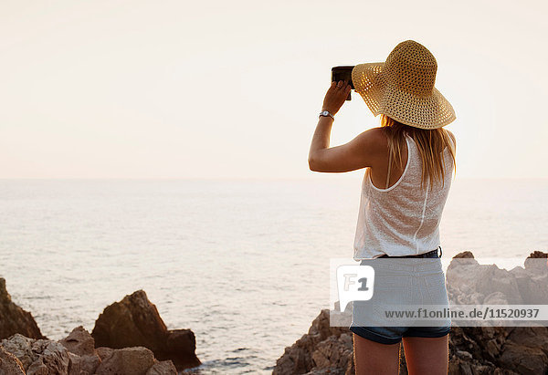 Rückansicht einer Frau  die mit einem Fernglas aufs Meer schaut  Ciutadella  Menorca  Spanien