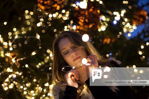 Junge Frau schaut auf Lichter in der Hand  Baum im Hintergrund