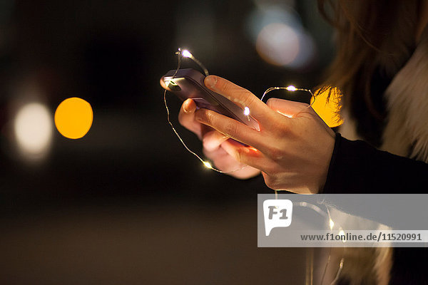 Young woman holding mobile phone and lights  close up of hand