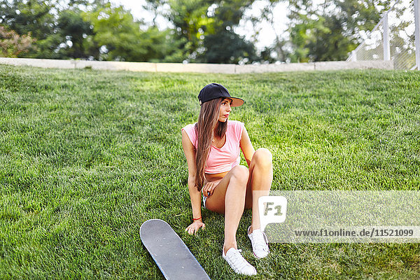 Junge Frau sitzt auf einem Grasrand  neben ihr ein Skateboard