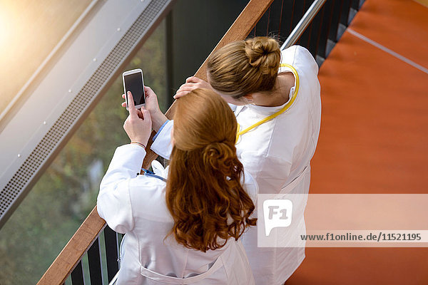 Hochwinkelansicht von zwei Ärztinnen auf dem Krankenhausbalkon mit Smartphone-Touchscreen