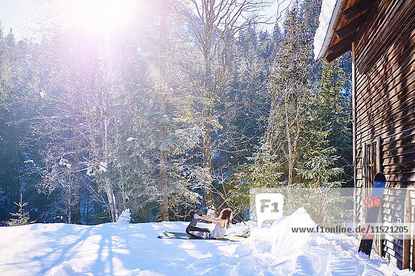 Frau übt Bogen-Yoga-Pose bei Blockhütte im Schnee  Österreich