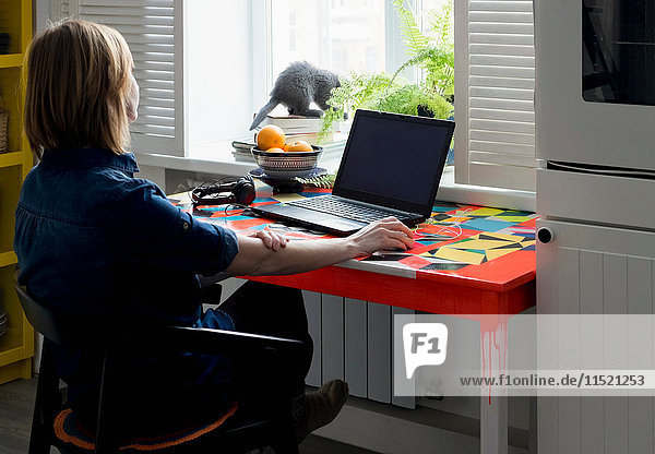 Woman sitting at table watching kitten on windowsill