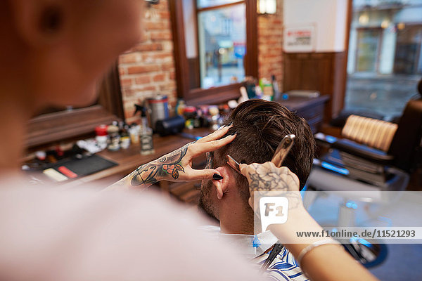 Hairdresser shaving customer's hair with straight razor