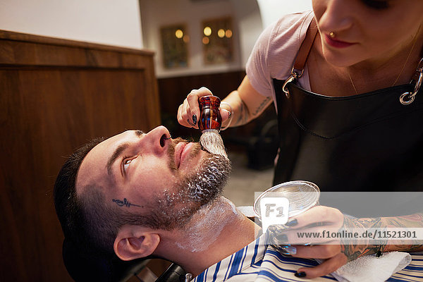 Woman applying shaving cream to man's beard