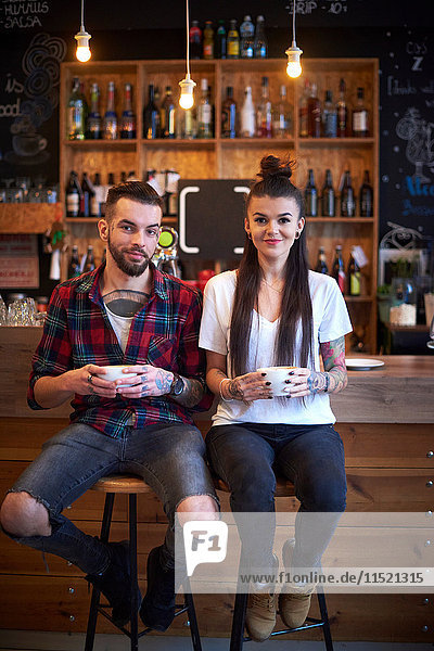 Paar sitzt nebeneinander auf Hockern im Café und schaut lächelnd in die Kamera