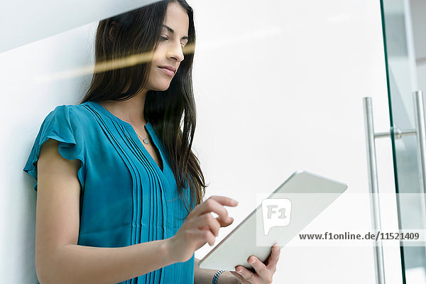 Fensteransicht einer jungen Geschäftsfrau mit digitalem Tablet-Touchscreen am Büroeingang