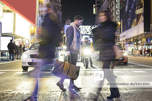 Mann mit Tasche und Handy überquert nachts eine Straße