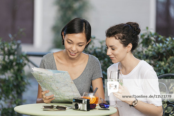 Zwei junge Frauen schauen gemeinsam auf die Karte im Straßencafé
