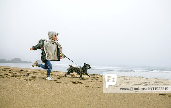 Fröhliches Mädchen mit Hund am Strand an einem nebligen Wintertag