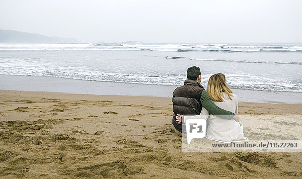 Couple in love sitting on the beach in winter