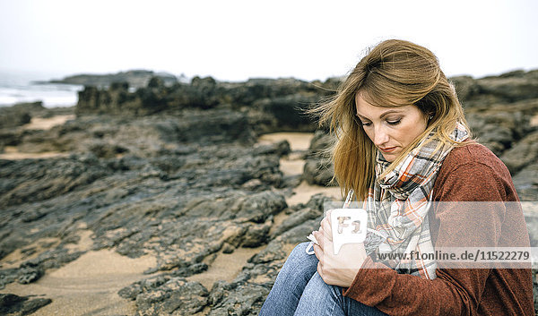 Frau mit Notizbuch auf Felsen am Strand im Winter