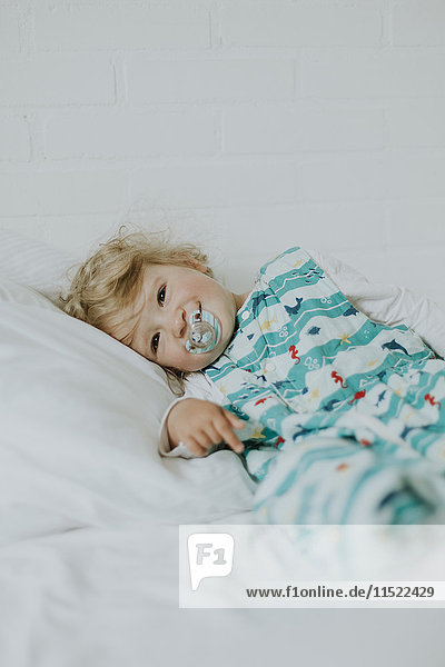 Kleines Mädchen mit Schnuller im Bett liegend