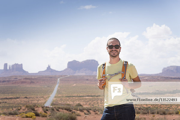 USA  Utah  Porträt eines lächelnden Mannes mit Rucksack und Sonnenbrille auf dem Weg zum Monument Valley