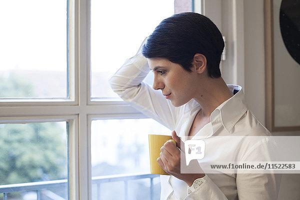 Woman holding cup of coffee looking out of window