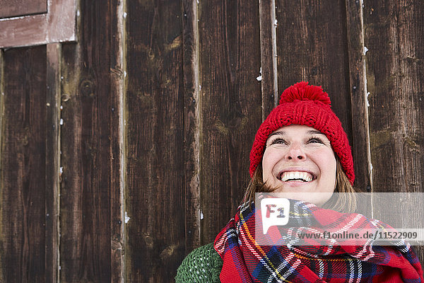 Porträt einer lächelnden Frau mit rotem Pudelhut im Winter nach oben schauend