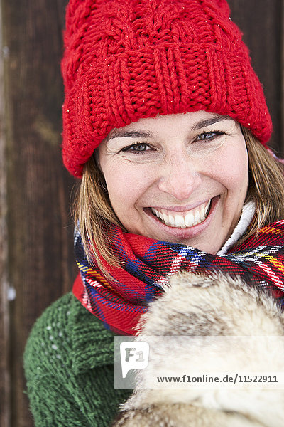 Porträt einer glücklichen Frau mit rotem Bommelhut im Winter