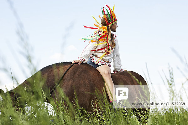 Mädchen mit Federkopfbedeckung Reitpferd auf der Wiese