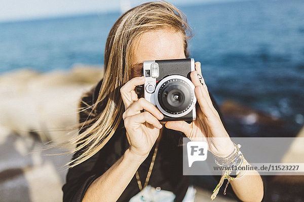 Junge Frau fotografiert mit altmodischer Kamera an der Strandpromenade